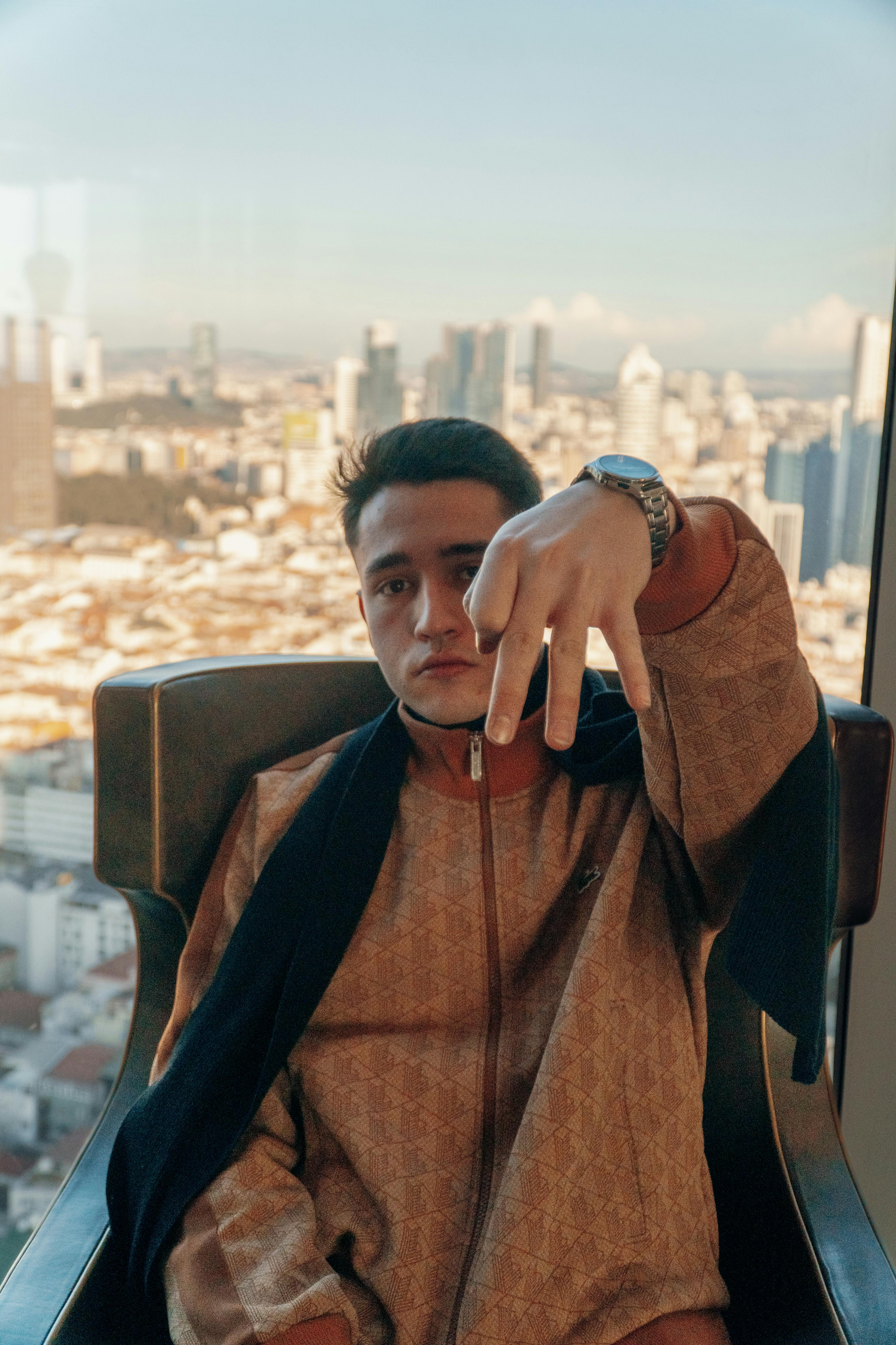 Young man sitting in a modern armchair enjoying a cityscape view from a high-rise apartment.
