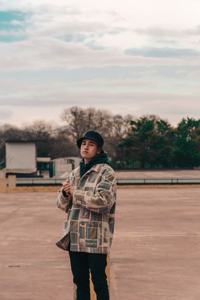 Fashionable young man wearing a stylish coat and hat in an outdoor setting.