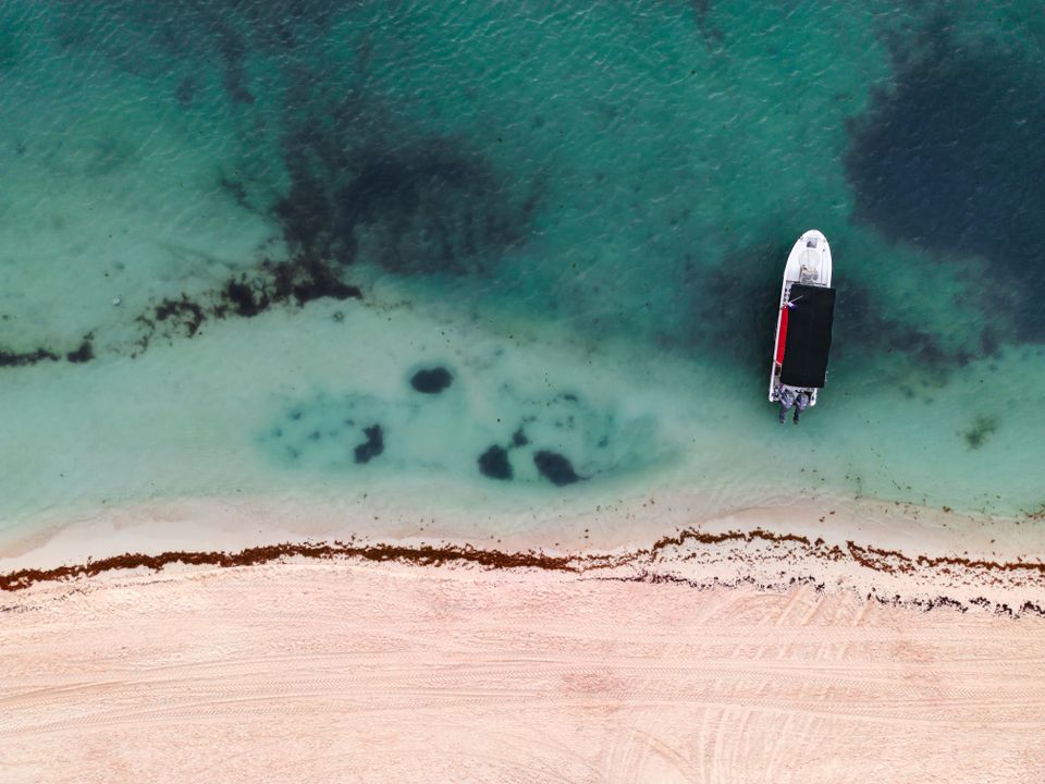 Aerial view of a small boat anchored near a sandy shoreline in shallow turquoise water