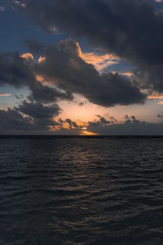 A dramatic view of the ocean at sunset with storm clouds gathering on the horizon.