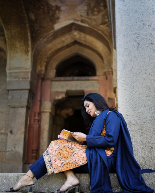 Elegant woman in traditional attire reading on ancient steps in Delhi.