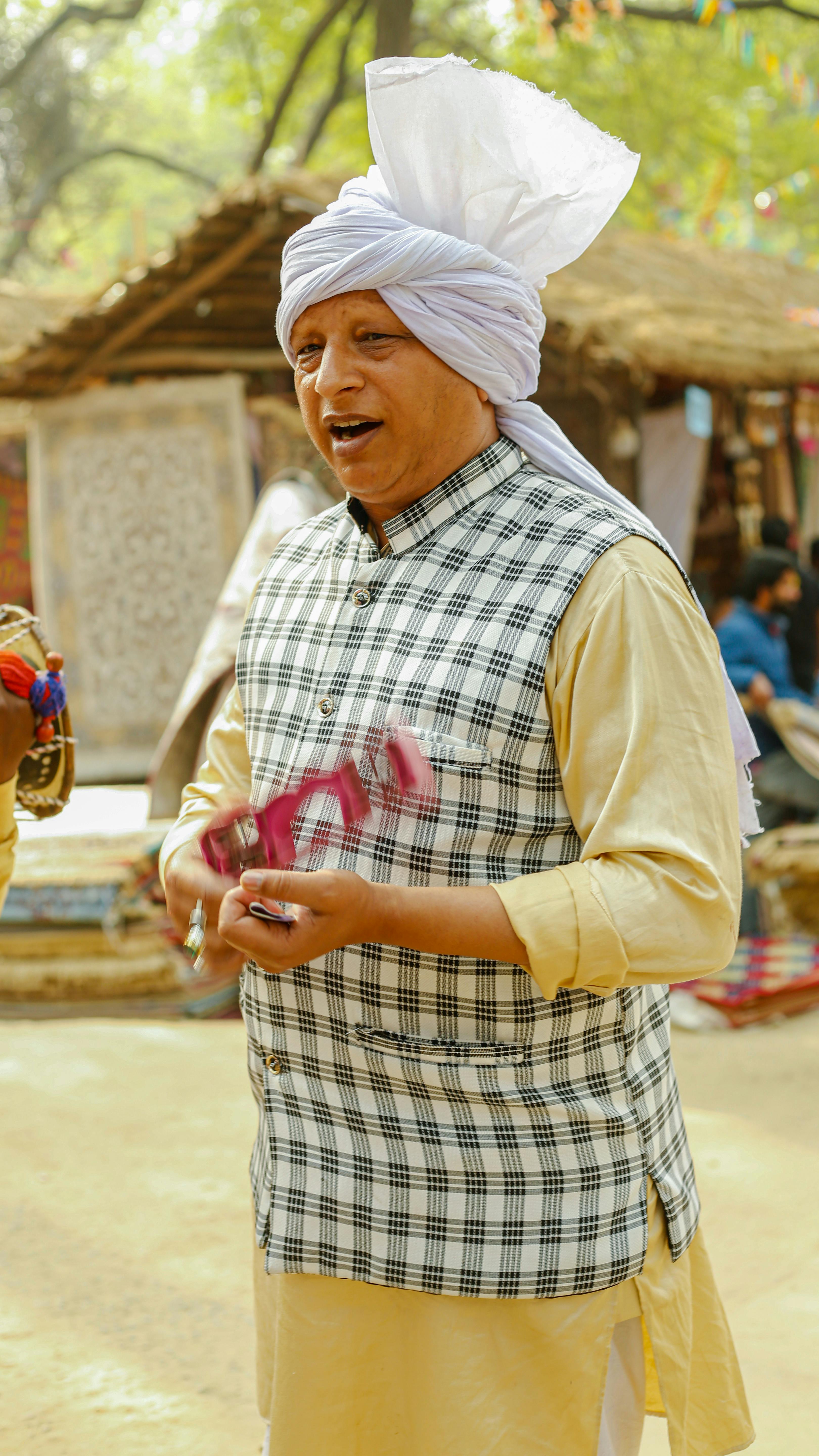 South Asian man in traditional attire holding a musical instrument at an outdoor market.