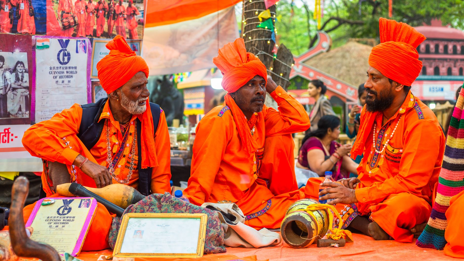 Three Indian snake charmers in vibrant orange attire at a cultural festival.