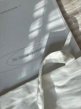 Natural light on an open planner titled 'The Startup Planner' with a white canvas bag.