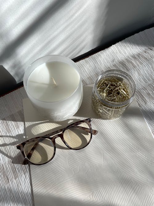 Jar of Golden Paper Clips Next to a Scented Candle and Eyeglasses