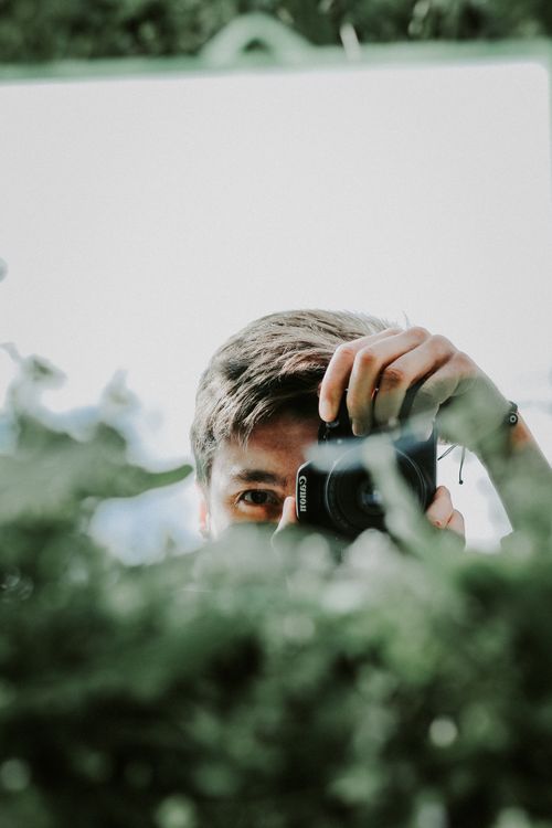 Free A young man captures his image with a camera in a reflective mirror, surrounded by greenery. Stock Photo