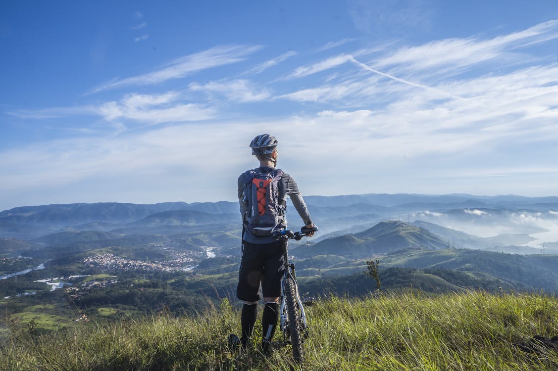 Free Biker Holding Mountain Bike on Top of Mountain With Green Grass Stock Photo