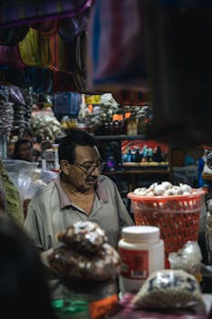 A man selling goods at a vibrant market stall, surrounded by diverse merchandise.