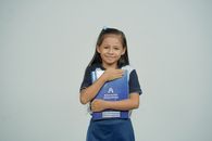 A young girl smiles while holding her school notebook, representing joy in education.