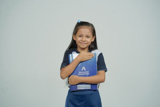 A young girl smiles while holding her school notebook, representing joy in education.