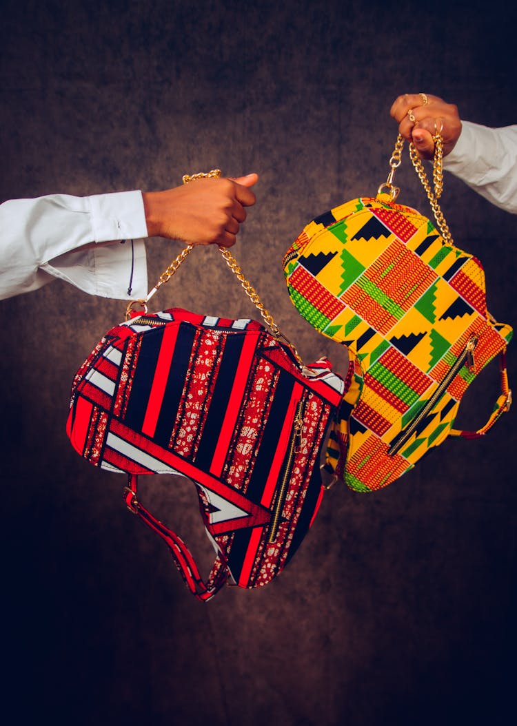 Hands Presenting Handbags In Shape Of Africa Decorated With Traditional Patterns