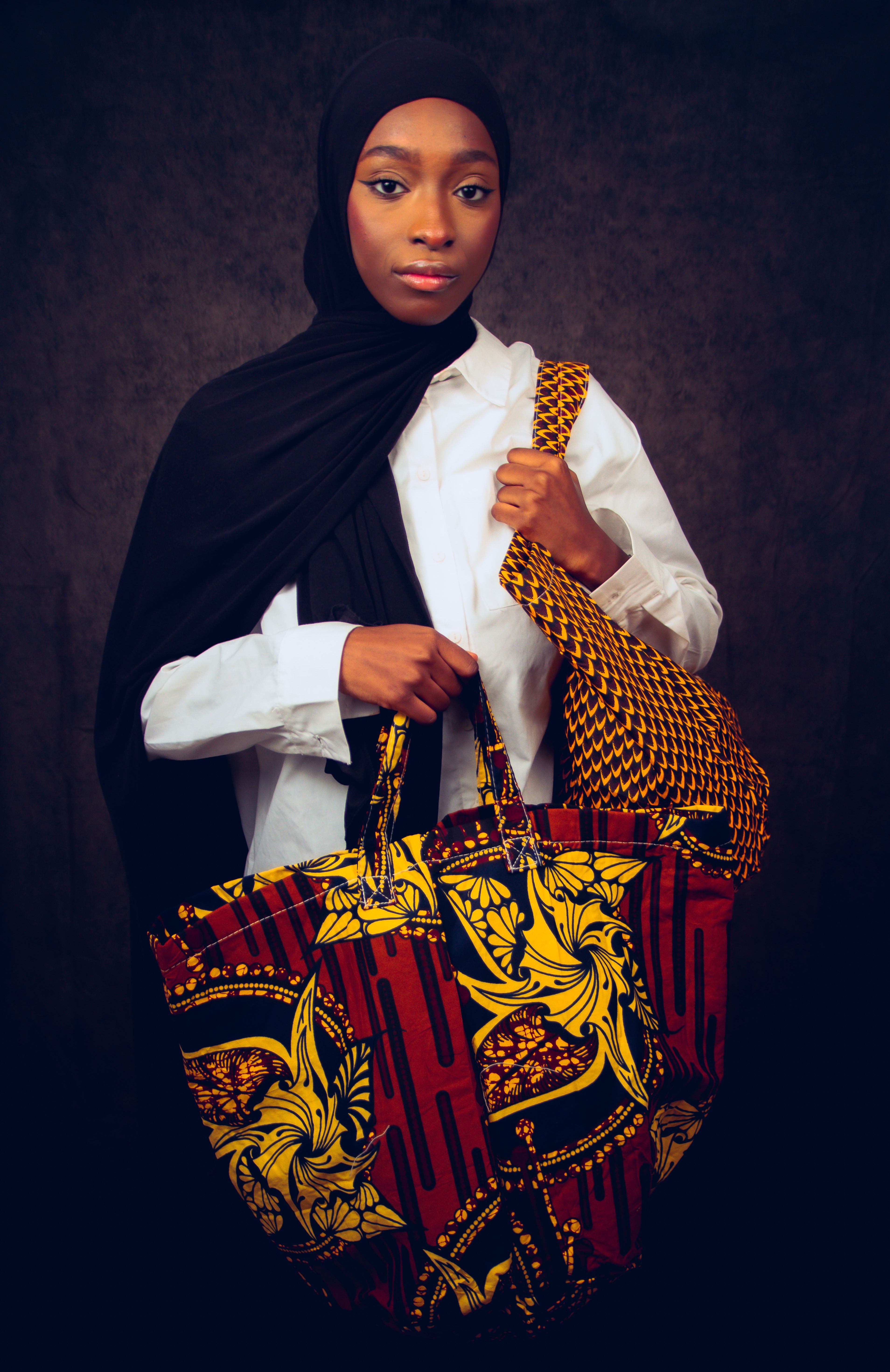 Portrait of a stylish hijabi woman wearing a white shirt and holding vibrant, patterned tote bags. - best handbag for different occasions