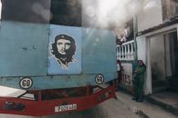 A vibrant urban scene featuring a truck with a mural of Che Guevara and local people.