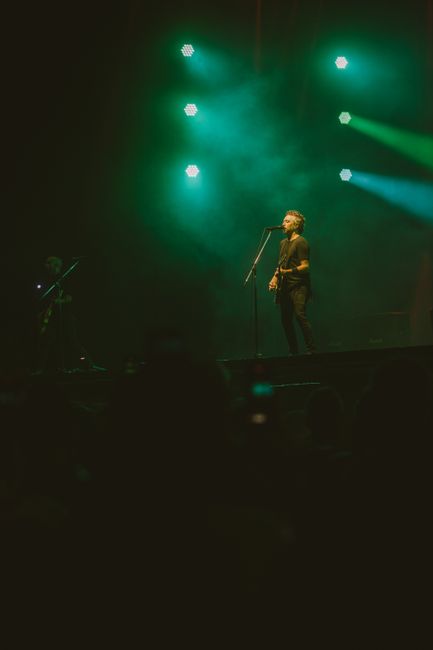 Energetic rock band on stage with green lighting and electric guitars during a night concert.