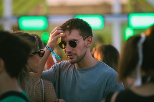 Man wearing sunglasses at a lively outdoor festival during daylight.