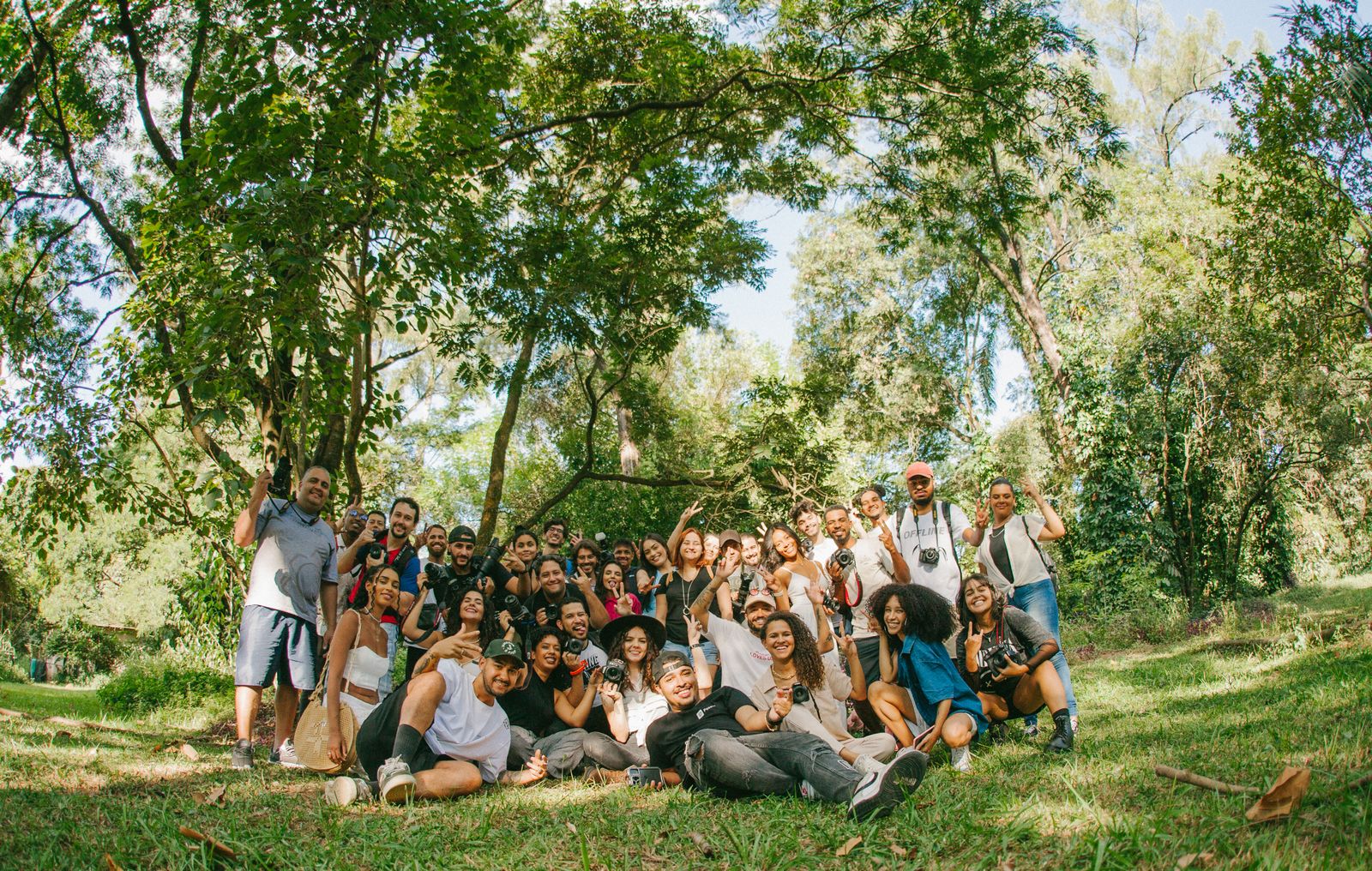 A large, diverse group of friends of different ages and backgrounds smiling together in a sunny green park