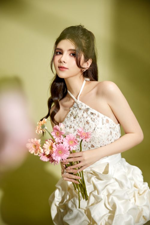 Free A young woman in a white dress holding a bouquet of pink flowers against a green background. Stock Photo