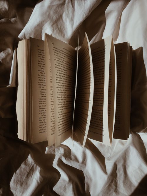 Free A vintage book with open pages lying on a white linen fabric creating a cozy still life scene. Stock Photo