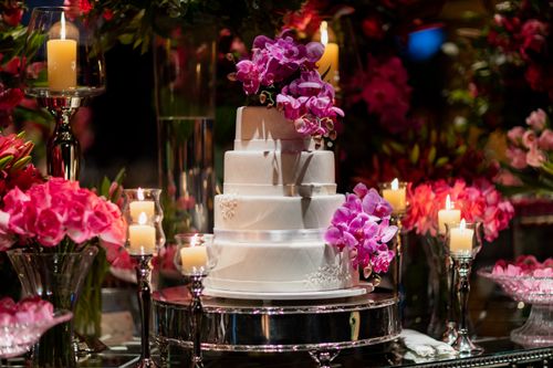 Free Beautiful three-tier wedding cake adorned with pink orchids and surrounded by candles and floral arrangements. Stock Photo