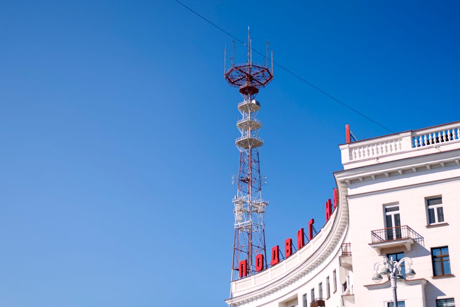 A clear view of a rooftop with a tall antenna tower against a bright blue sky, capturing urban architecture.