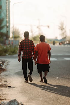Two men walking down a city road during sunset, casting long shadows.