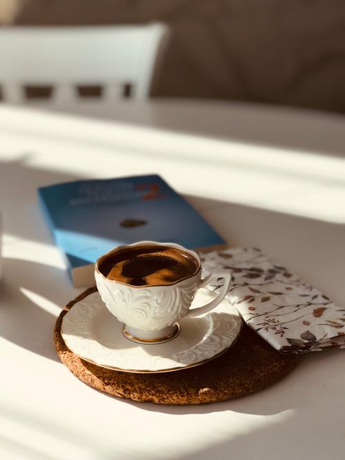 Free A porcelain cup of espresso beside a book on a sunny table. Stock Photo