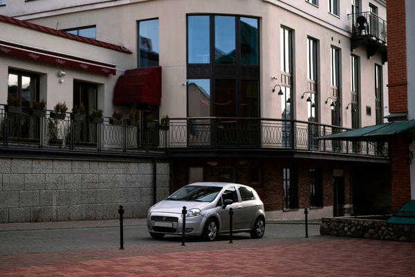 Silver compact car parked outside a stone apartment building. Photo by Vitali Adutskevich on Pexels
