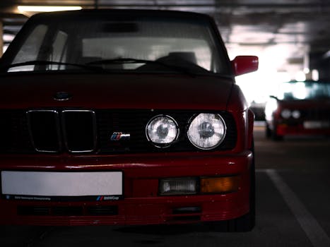 Front view of a vintage red BMW M series car in a dimly lit parking garage.