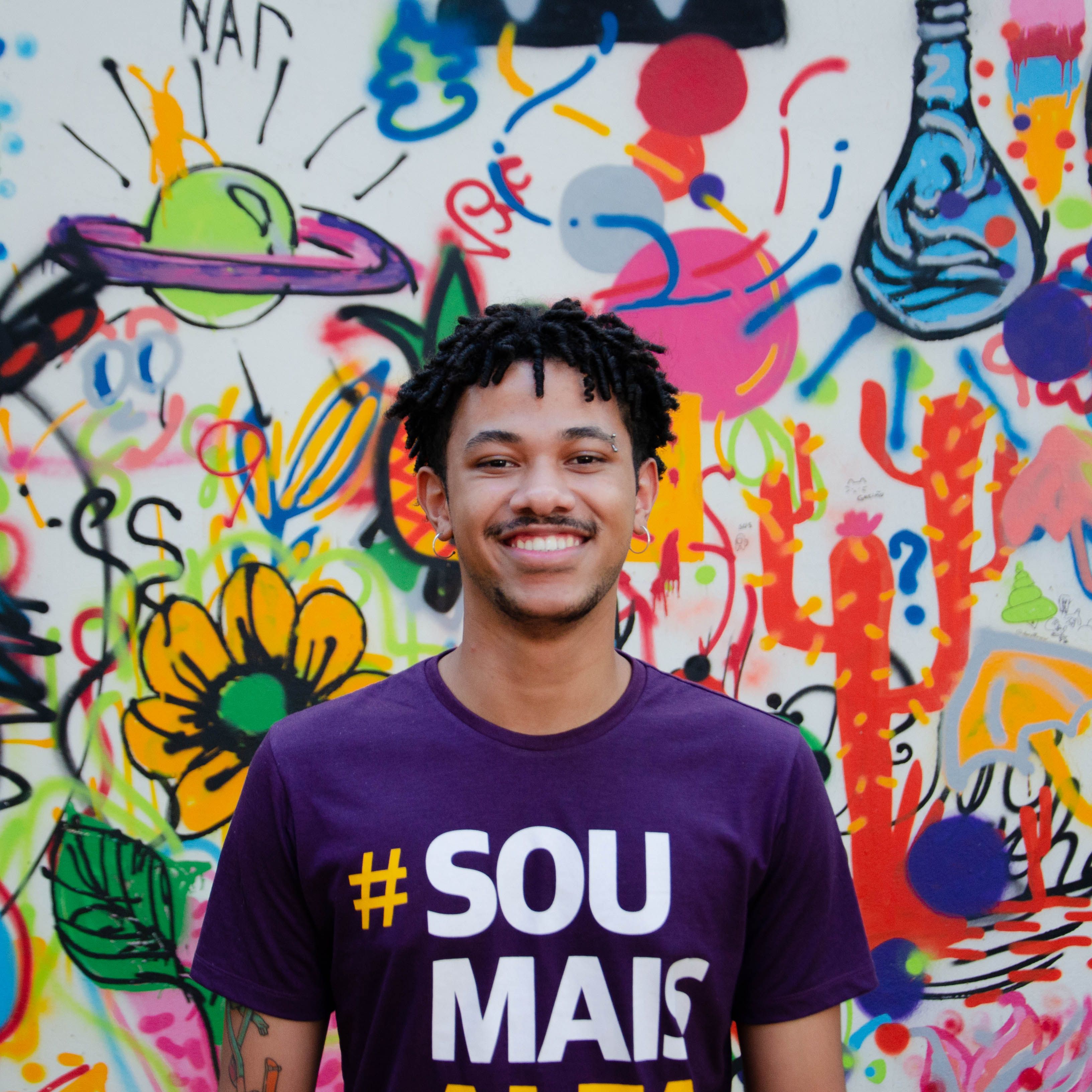 Smiling man posing in front of colorful graffiti wall. Urban art scene.