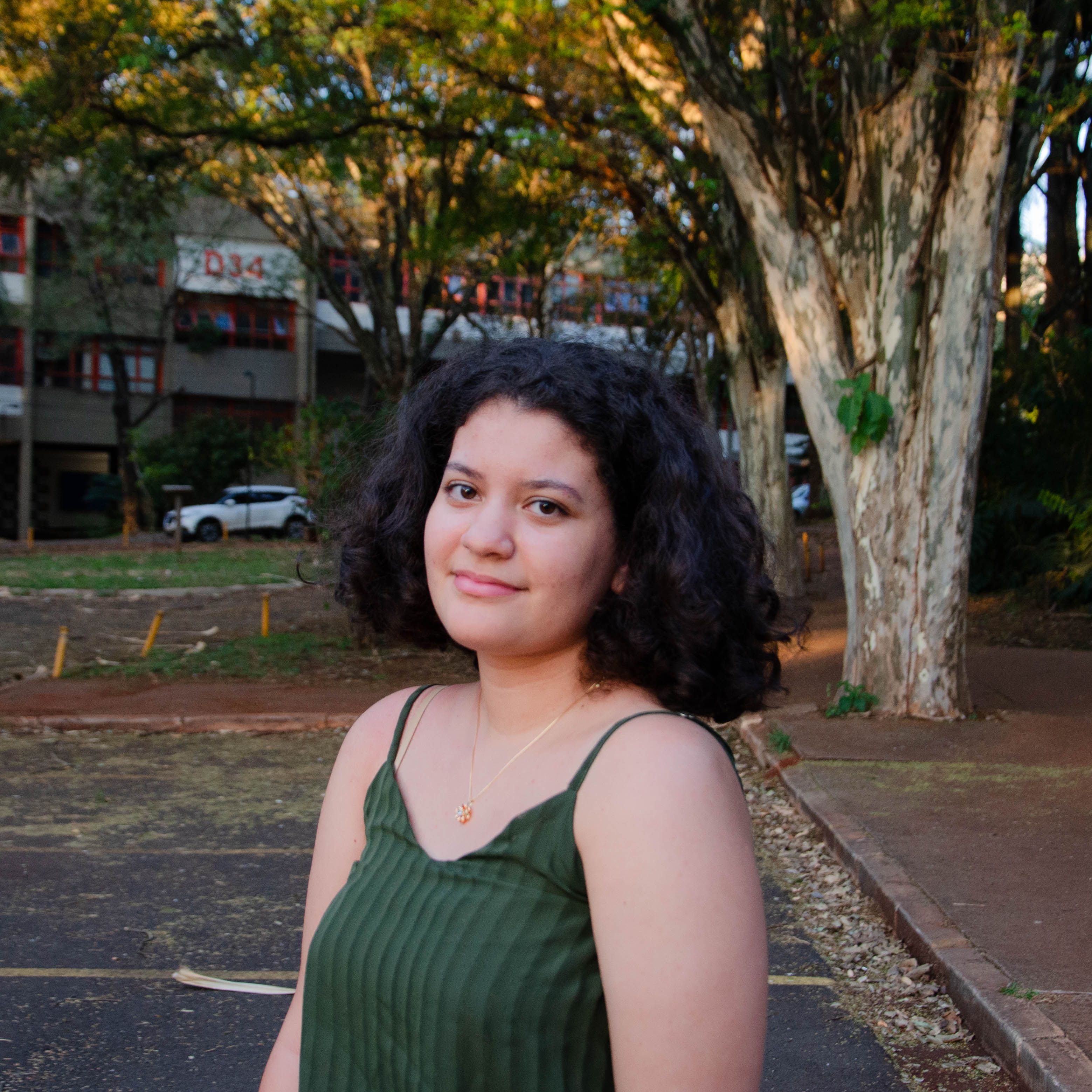 Portrait of a young woman in a green dress standing outdoors by trees.