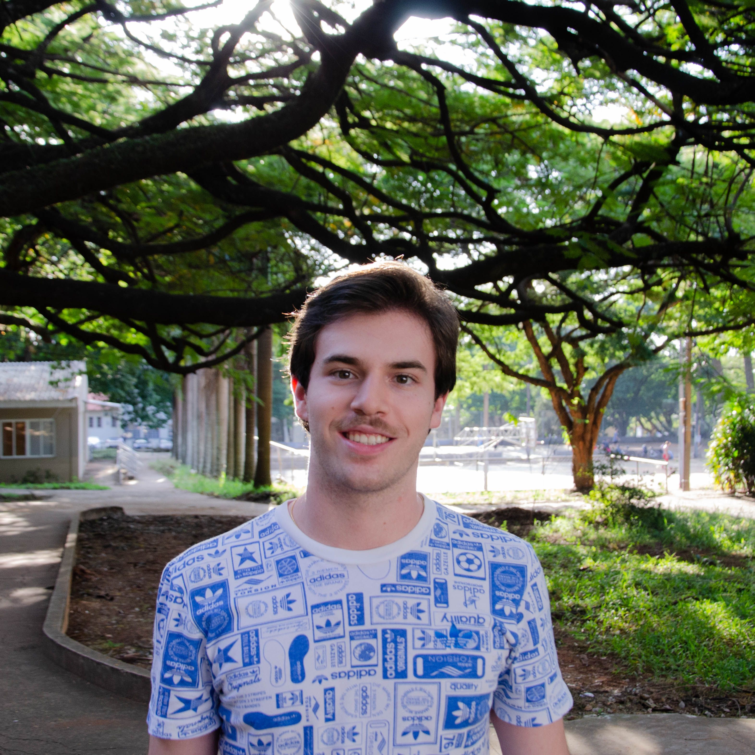 Young man smiling under lush tree canopy in a sunny park setting. Vibrant and lively atmosphere.