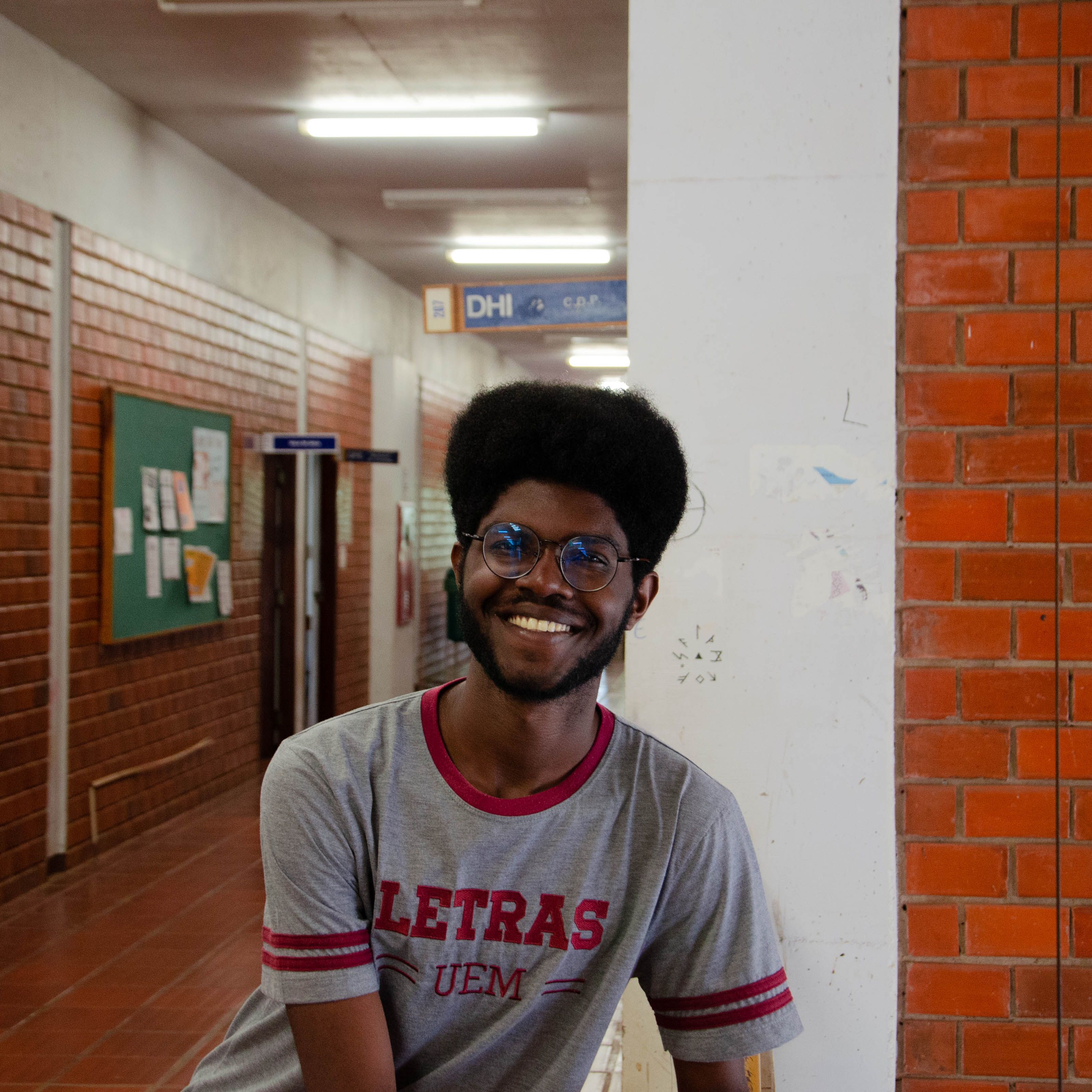 Cheerful student with glasses leaning in a university hallway at day.