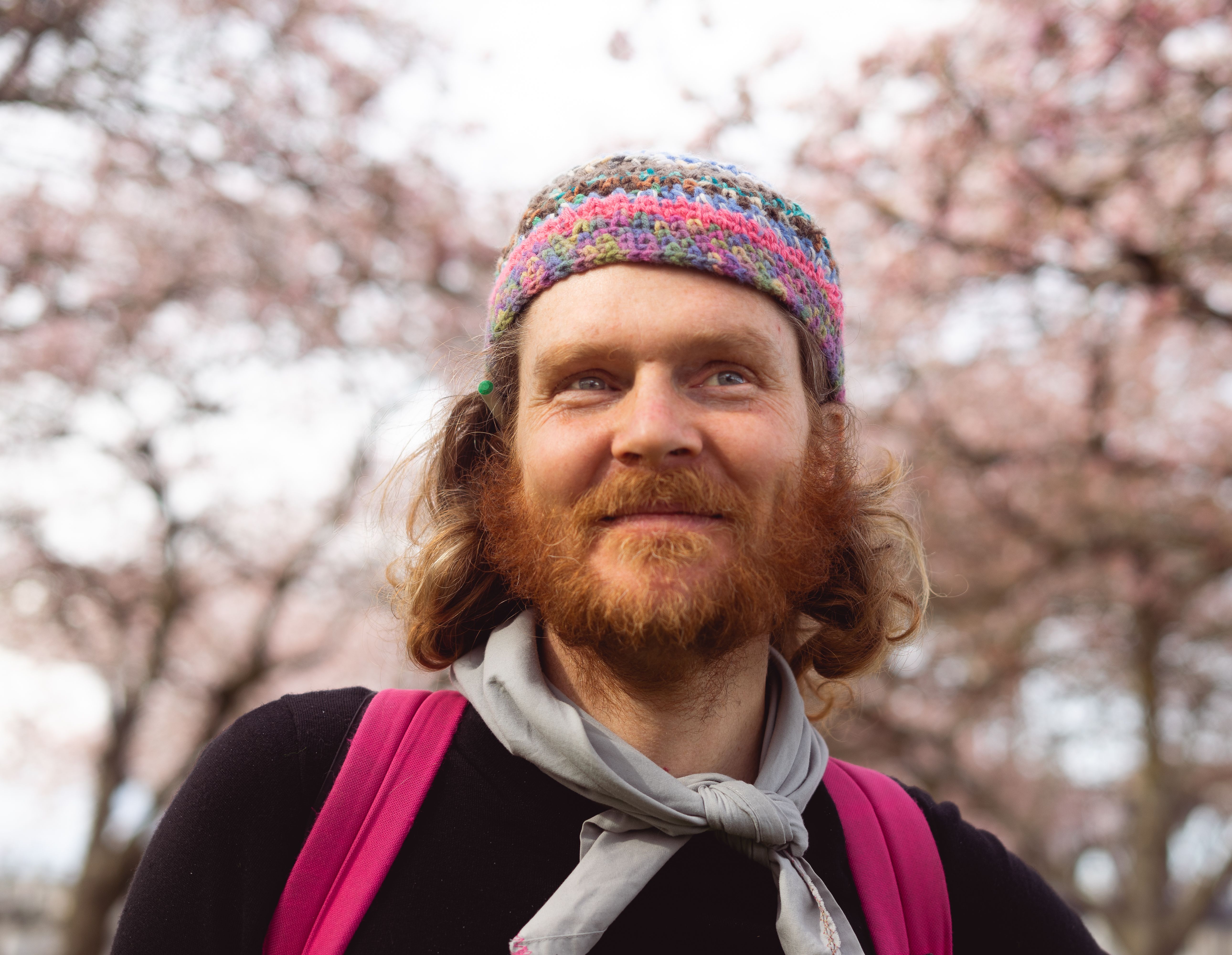 Smiling man in a knitted hat enjoying cherry blossoms in a Portland park.