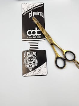 Close-up of gold barber scissors and El Patron marketing sticker on white background.