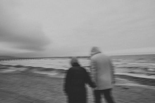A couple holding hands walking on a windy beach in black and white.