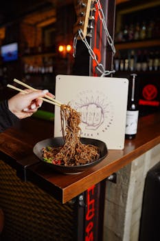 Appetizing noodles being lifted with chopsticks in a trendy urban restaurant setting.