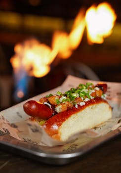 Delicious gourmet hot dog topped with onions and sauce, set against a dramatic fiery background.