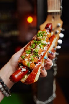 Close-up of a gourmet hot dog with toppings, held by hand, indoors.