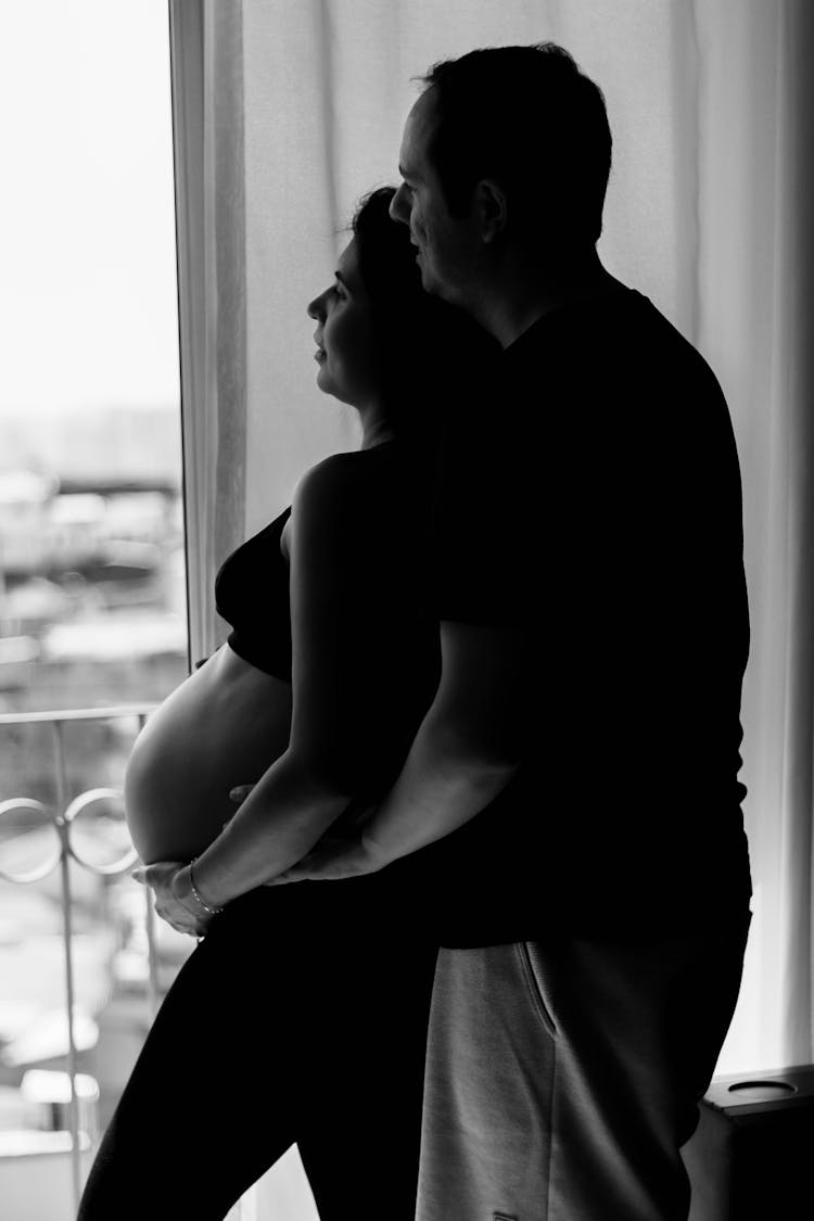 Black And White Photo Of A Man Embracing His Pregnant Wife 