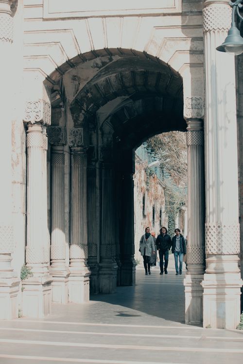 Free Three people walking through a historic architectural archway in an urban setting. Stock Photo