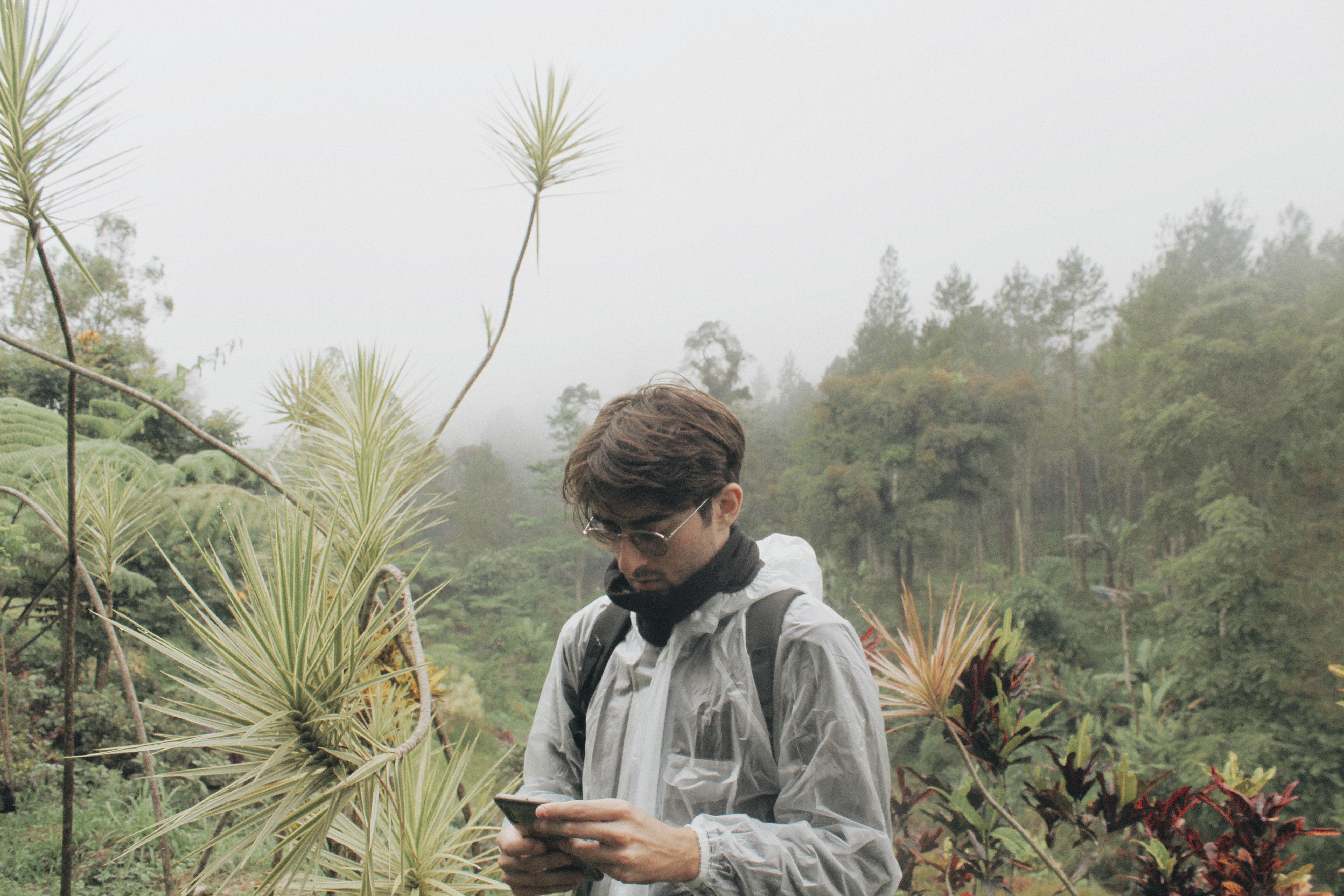 A man in a raincoat using a phone in a misty tropical rainforest setting