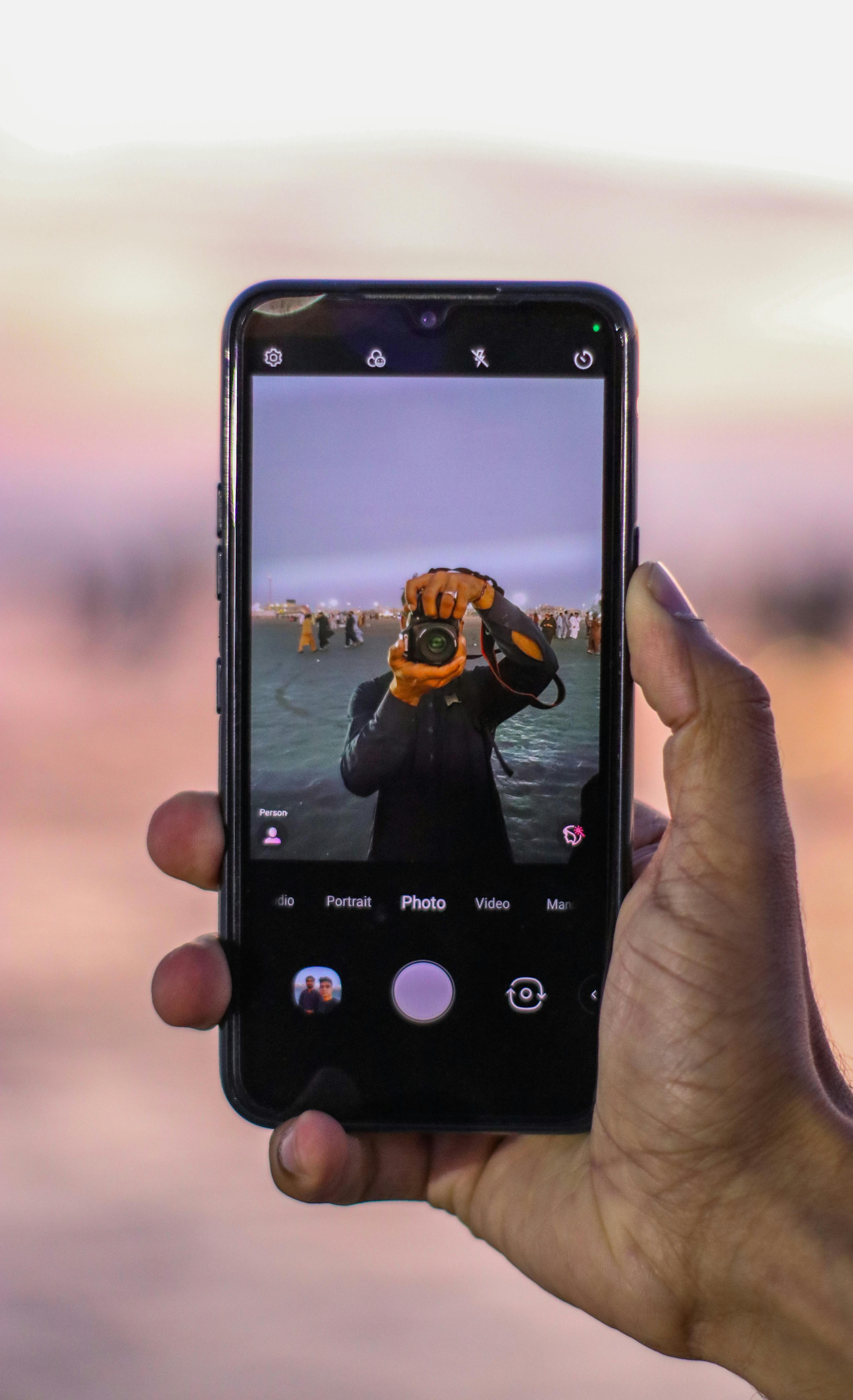 Free A photographer captures a scene through a smartphone displaying a vibrant photo. Stock Photo