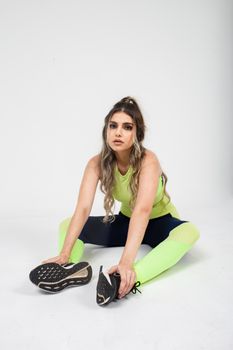 Young woman in neon sportswear stretching on a white background, studio shot.
