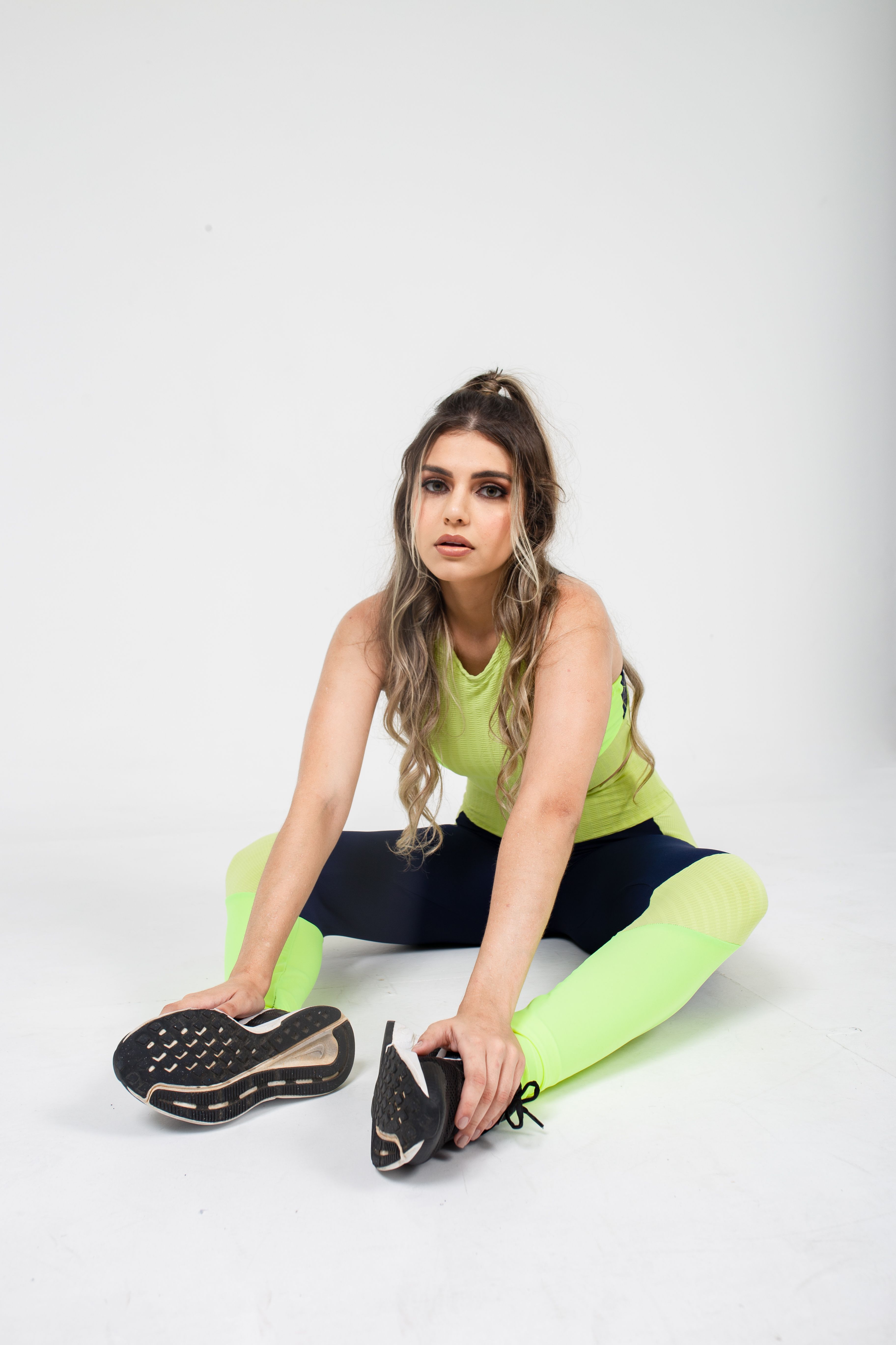 Free Young woman in neon sportswear stretching on a white background, studio shot. Stock Photo