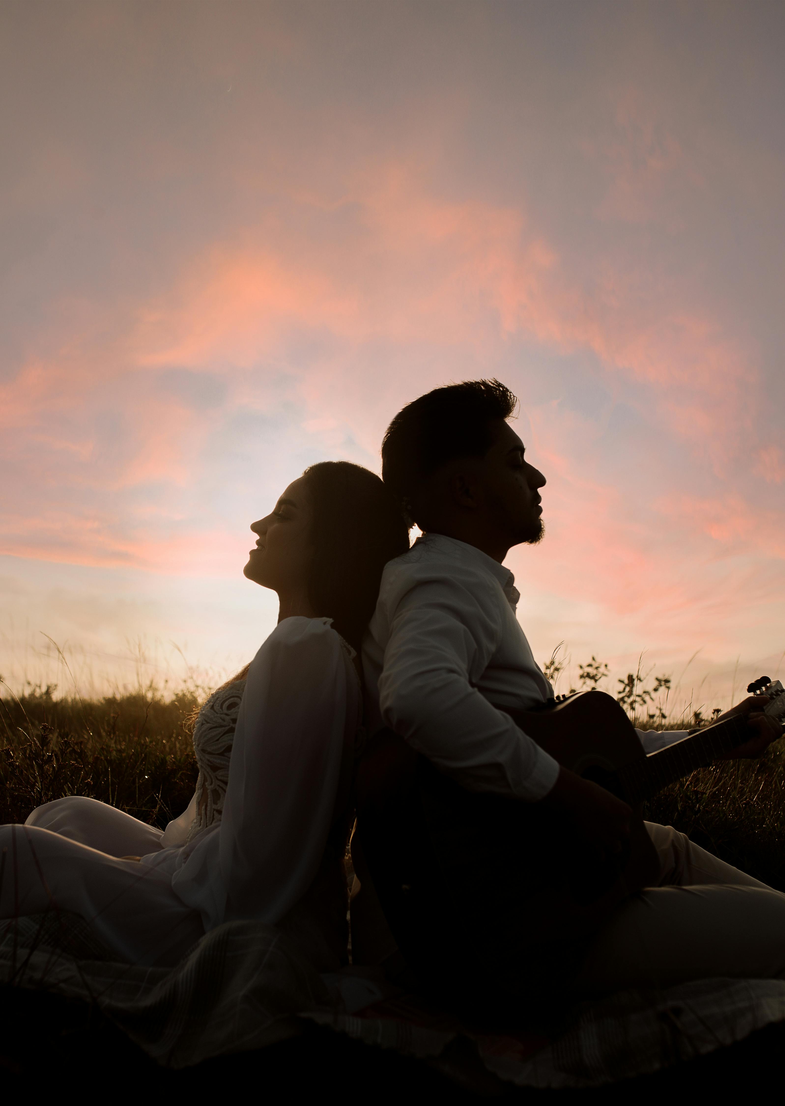 Silhouette of a Man and Woman Sitting Back to Back on a Field at Sunset