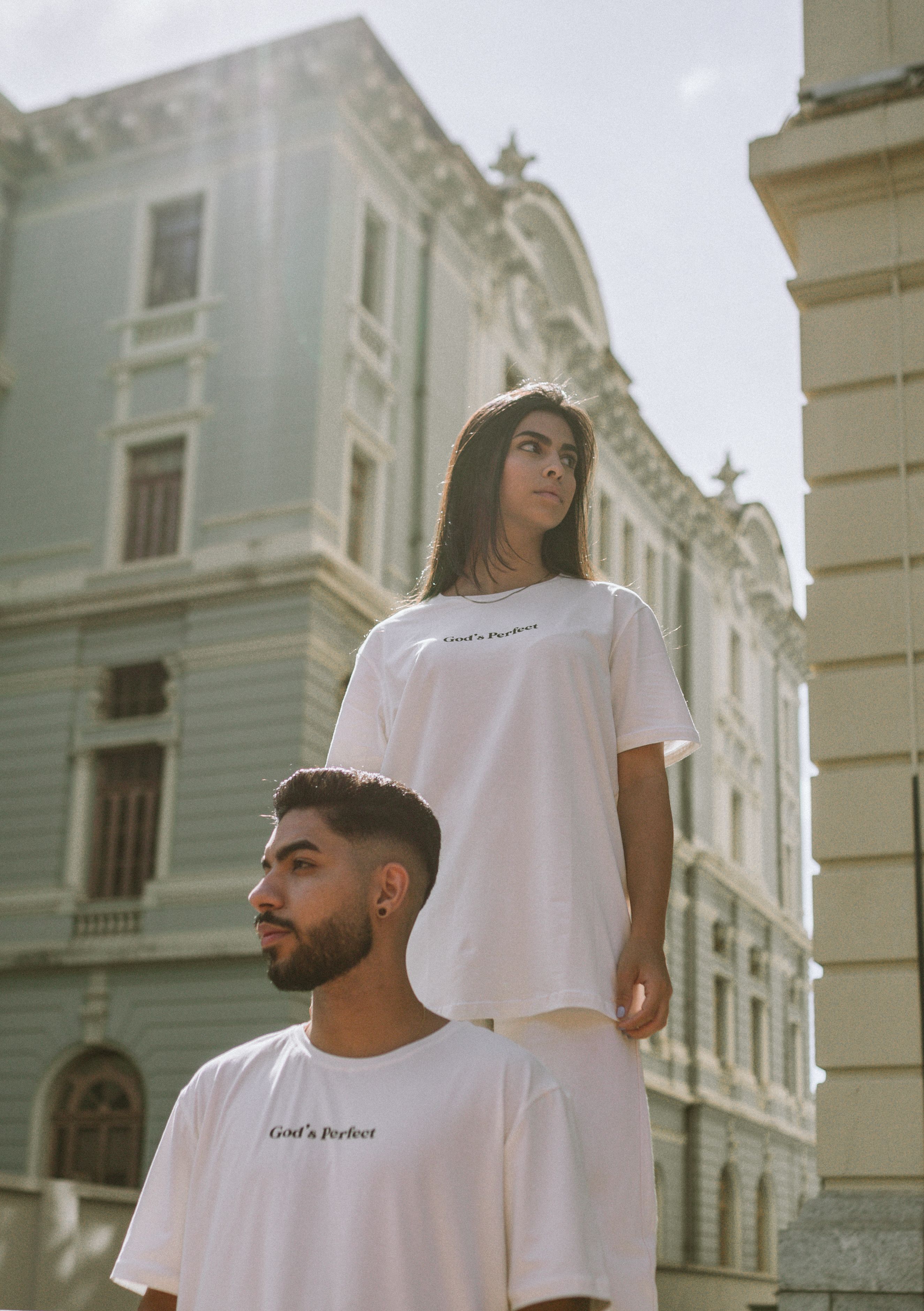 Duo fashion em camisetas brancas posando contra a arquitetura clássica da cidade.