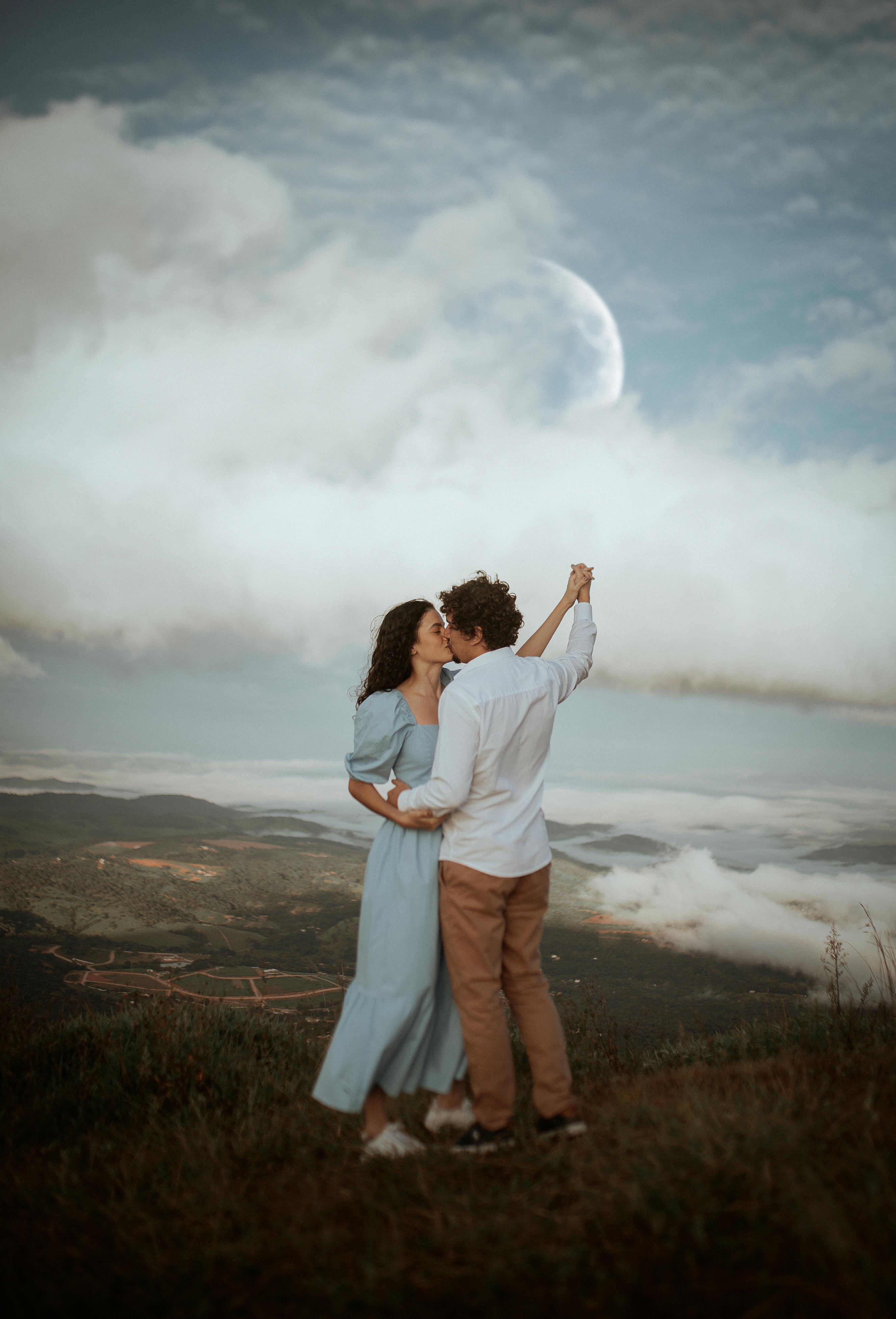 A couple embraces on a hilltop with a stunning moonlit backdrop.