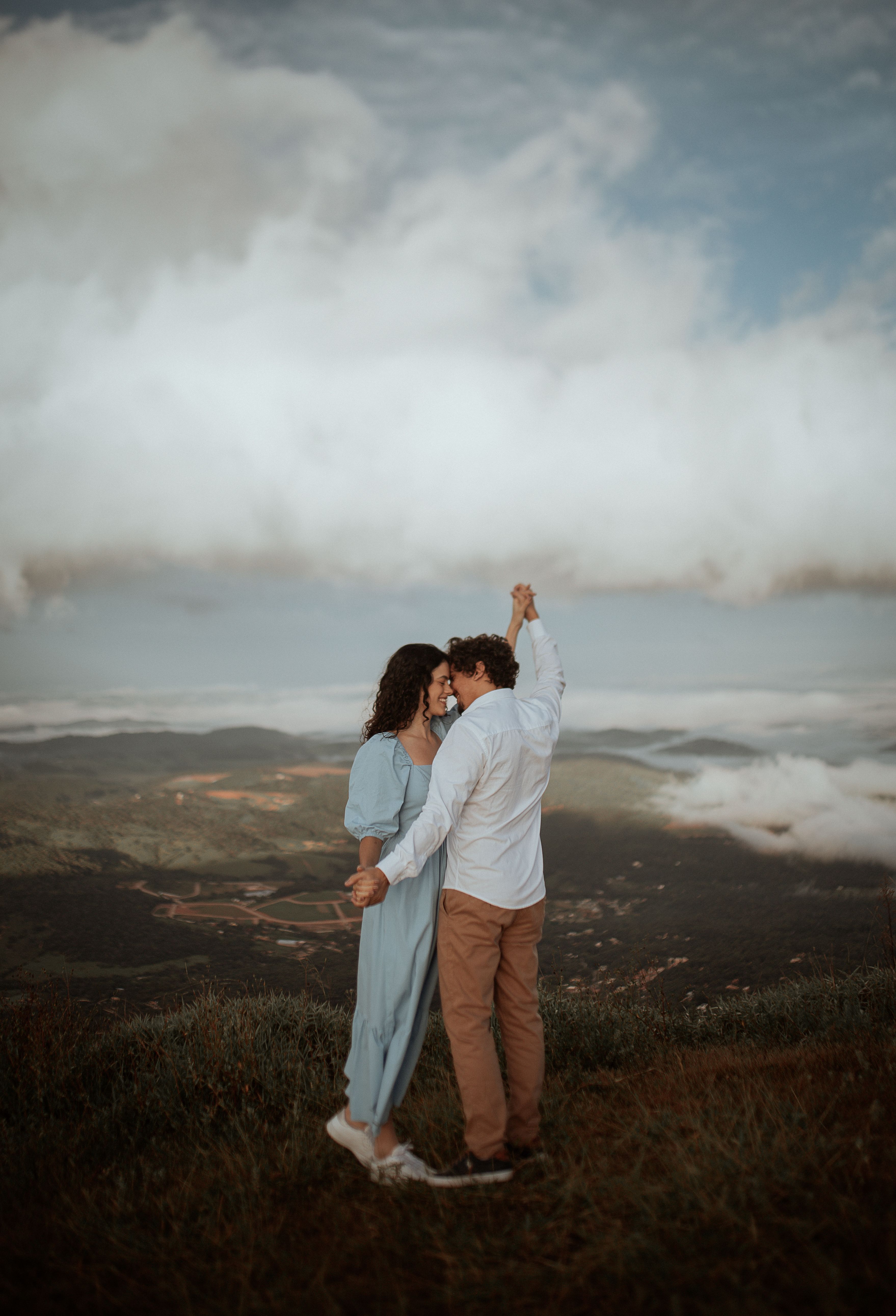Couple sharing a tender moment on a scenic mountaintop with clouds and landscape view.