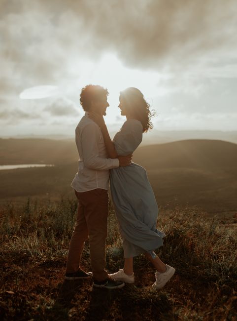 Couple embracing at sunset on a hill with scenic view, symbolizing love and serenity.
