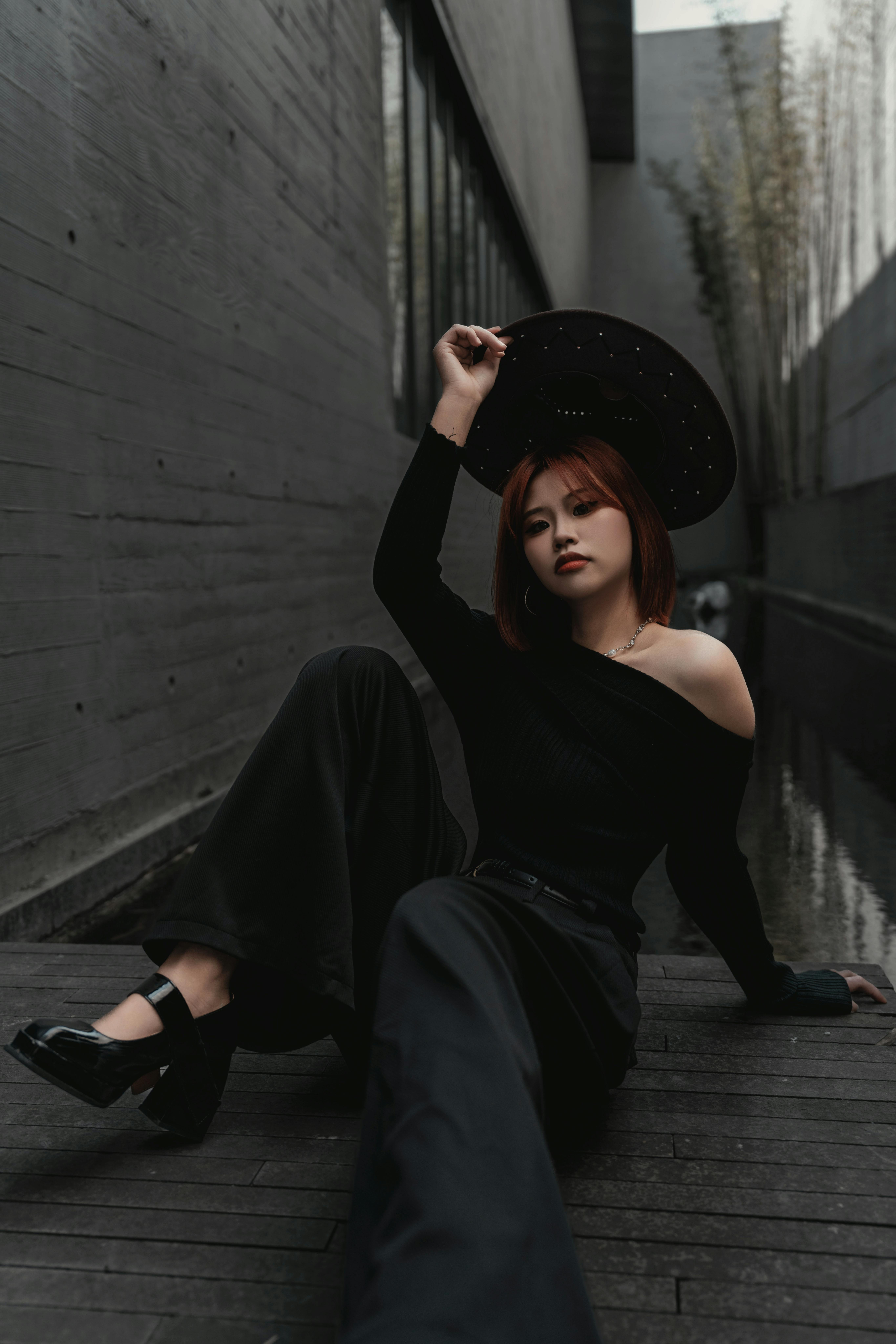 Fashionable woman in black outfit posing with hat in a modern architectural space.
